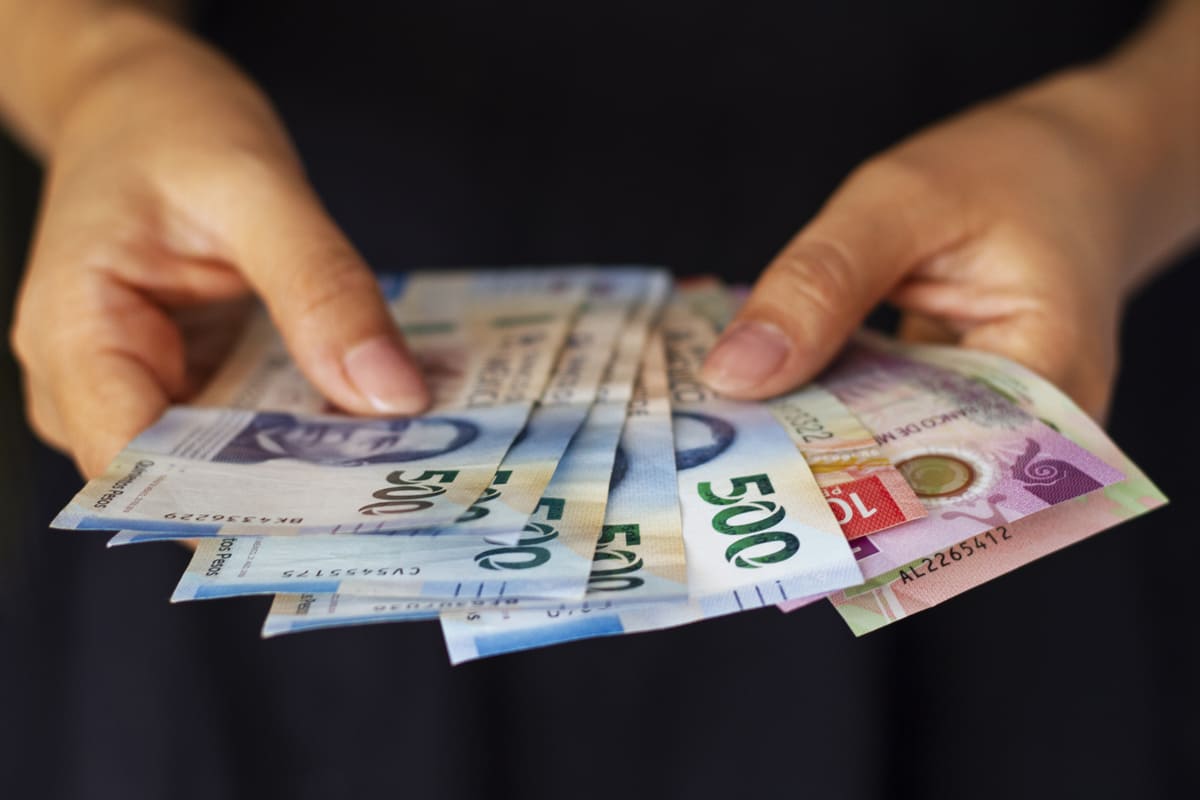 Manos sosteniendo billetes mexicanos.